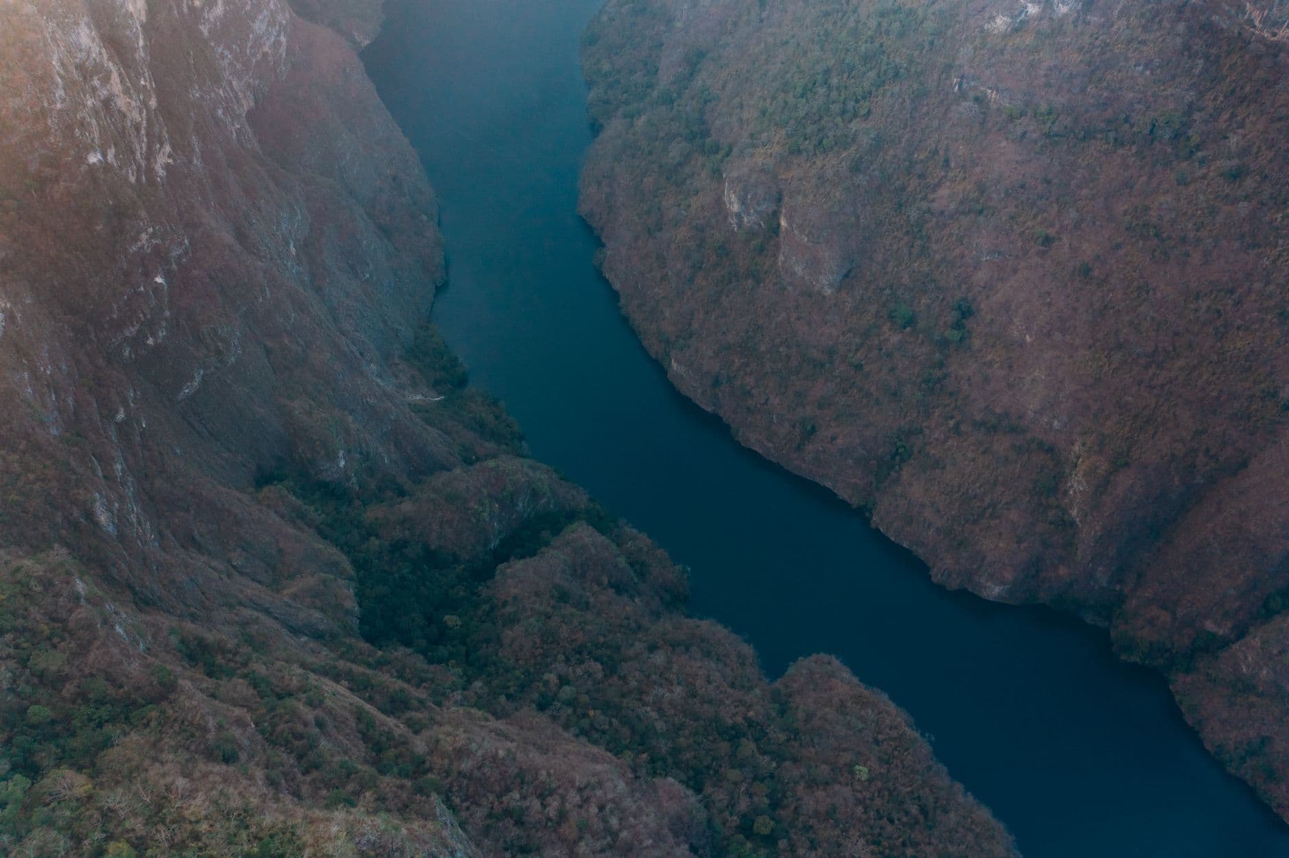 An aerial view of a deep blue river winding between mountain cliffs
